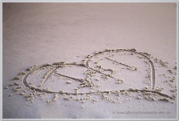 Close-up of a heart with the couple's initials drawn in pale beach sand