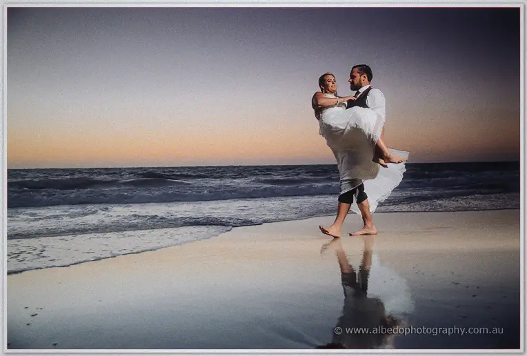 Troy sweeps Teigan off her feet on mirror-wet sand beneath a violet evening sky