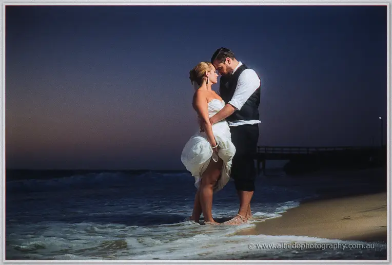 Foreheads touching, the couple linger in the shallows as the jetty fades into dusk behind them
