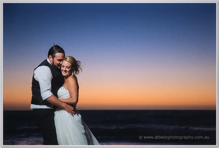 Troy wraps Teigan in a close hug, her hair loose in the breeze under an orange horizon