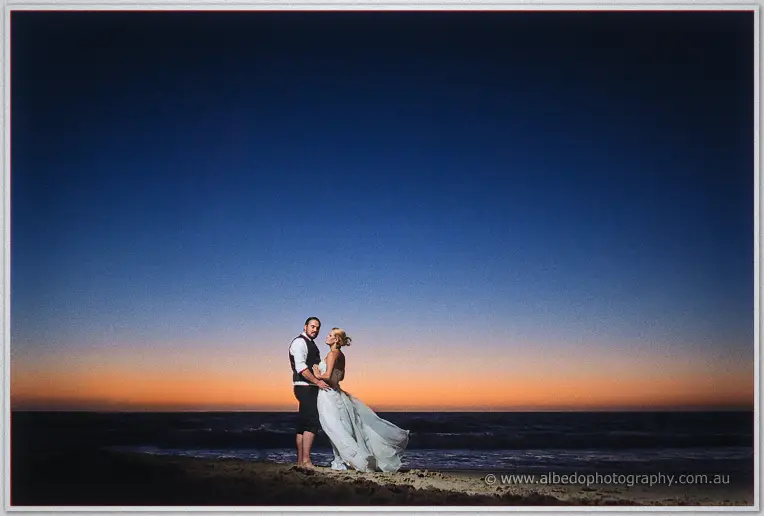 Wide dusk frame of the couple silhouetted small against a huge indigo sky on the sand