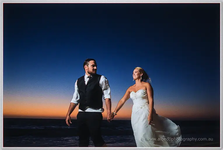 Hand in hand at nightfall, the couple stroll past the camera grinning in windblown formal wear