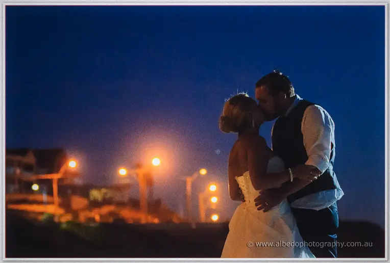Night kiss on the Hillarys foreshore with warm streetlights bokeh glowing behind the couple