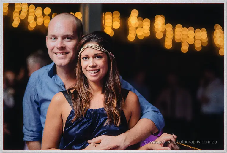 Guests smile under golden festoon lights, her jewelled headband catching the glow