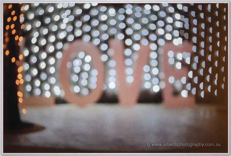 Soft-focus LOVE letters and fairy lights blur into bokeh across the reception room