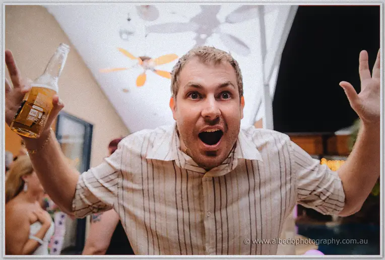 A wide-eyed guest in a striped shirt whoops with a beer bottle raised on the dance floor