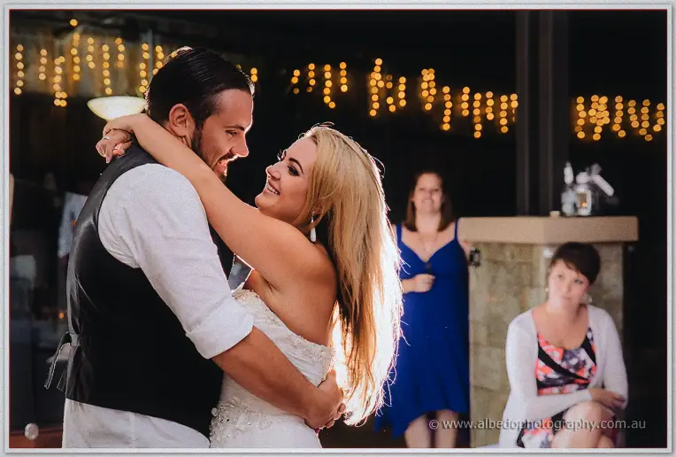 First dance cheek to cheek under warm fairy lights as guests watch from the bar
