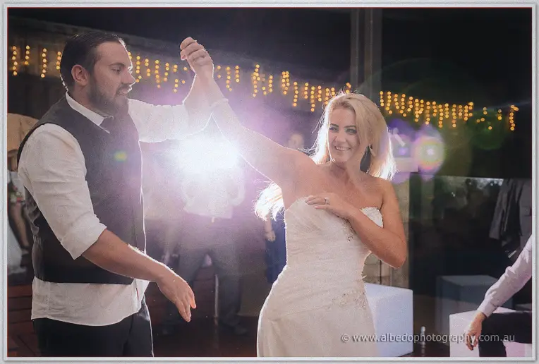 Troy twirls Teigan across the dance floor, lens flare sparking through the festoon lights