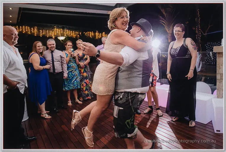 A man in a trilby lifts a delighted guest clean off her feet on the packed dance floor