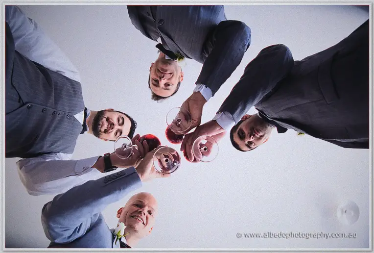 Michael and his groomsmen clink wine glasses over the camera in a huddle from below.