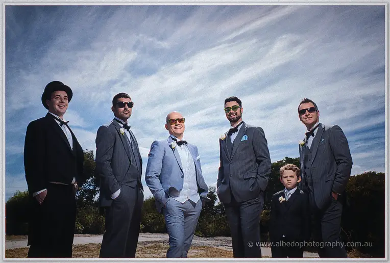 The groomsmen and page boy line up in shades beneath a dramatic cloud-streaked sky.