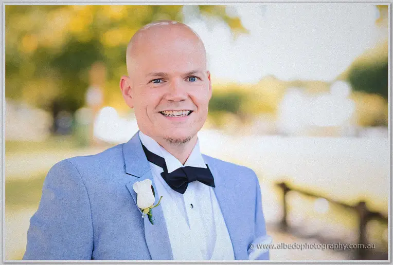 Michael beams in his pale blue suit and black bow tie under soft golden-hour trees.