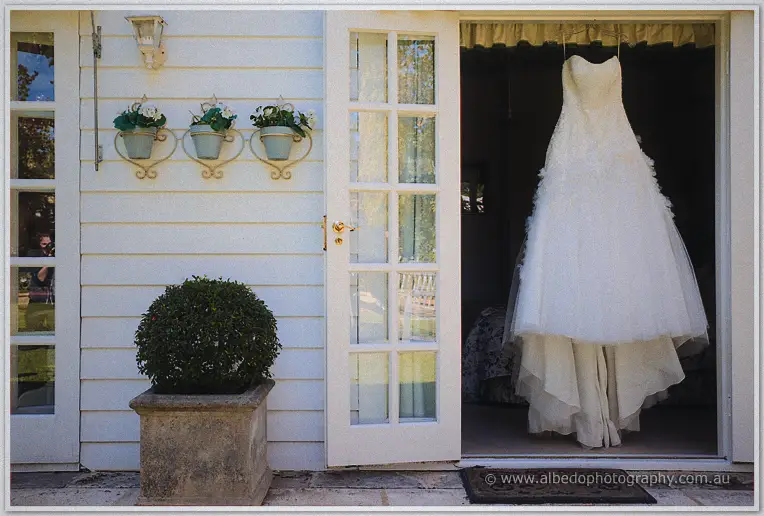 Jasmine's strapless lace gown hangs in an open doorway beside white weatherboard walls.