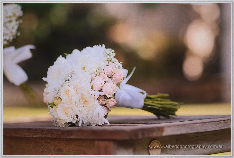 Jasmine's bouquet of cream and blush roses rests wrapped in ribbon on a timber bench.
