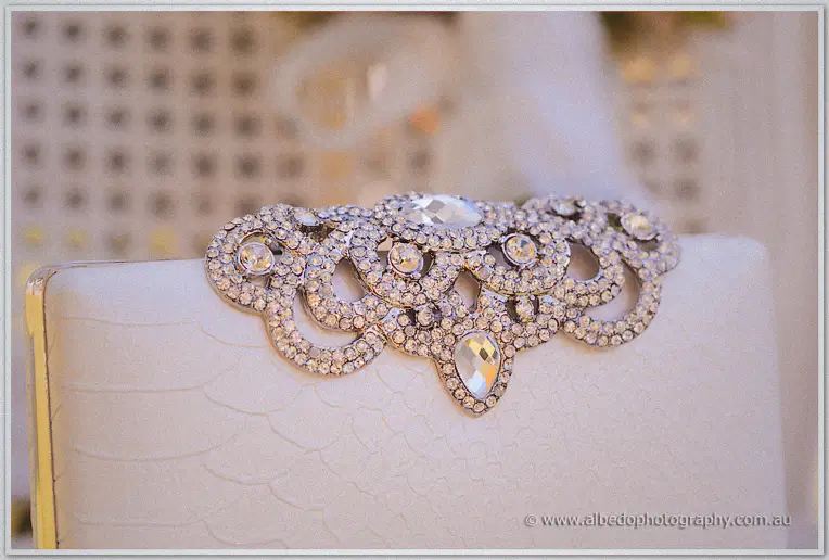 Close-up of a cream bridal clutch with a sparkling crystal brooch clasp, soft gold glimmering behind