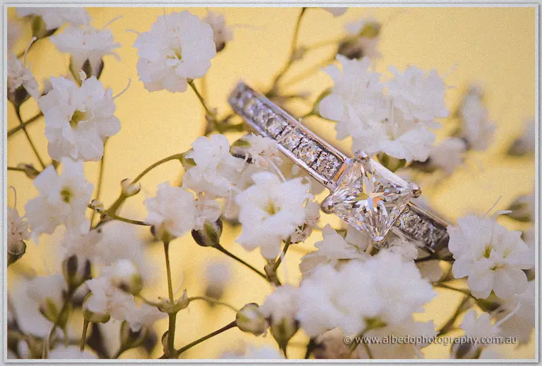 Princess-cut diamond engagement ring nestled in white baby's breath blossoms against a warm golden glow