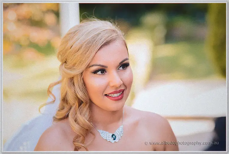 Outdoor portrait of bride Jasmine glancing sideways in dappled garden light, crystal necklace on her gown