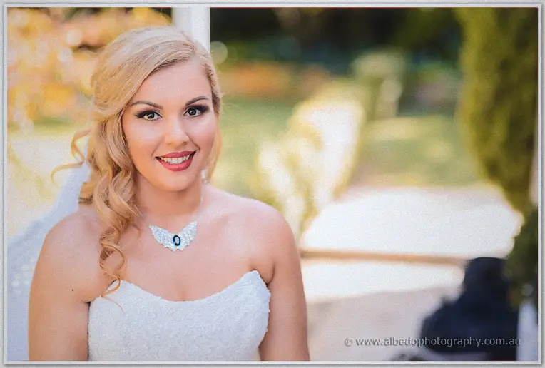 Bride Jasmine smiling at the camera in soft garden light, sapphire and crystal necklace on her lace gown