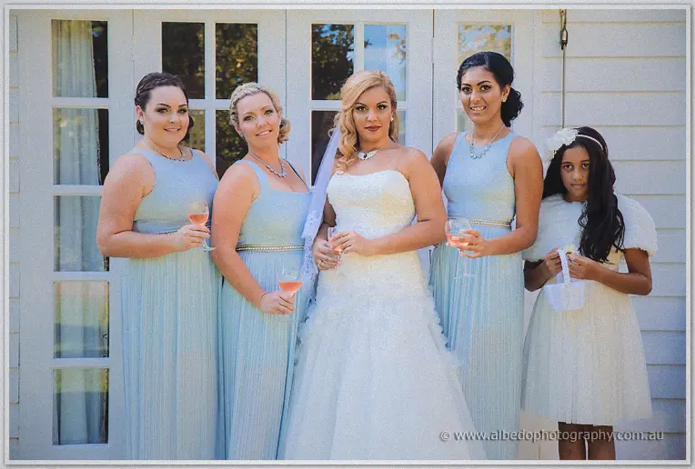 Bride Jasmine lined up with bridesmaids in powder blue and a flower girl in white outside French doors