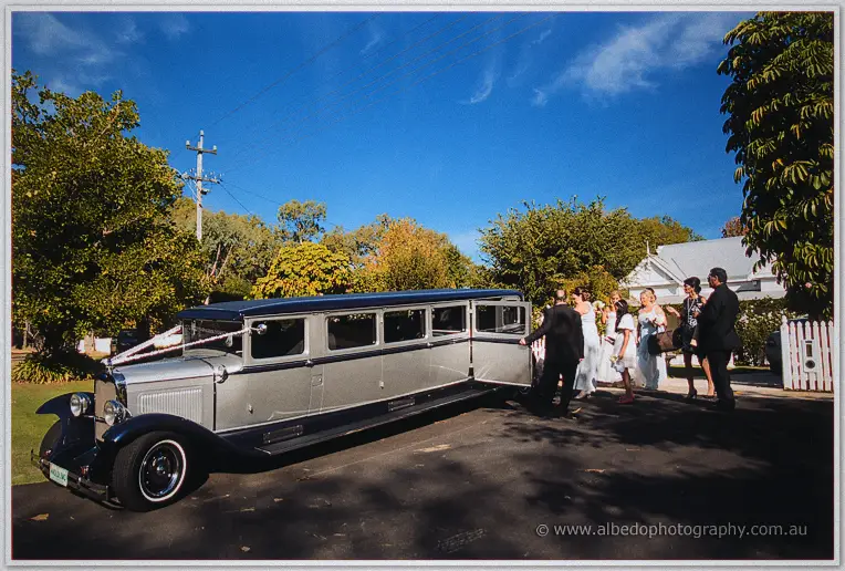 Silver and navy vintage stretch limousine with ribbon bow as the bridal party boards under a bright blue sky