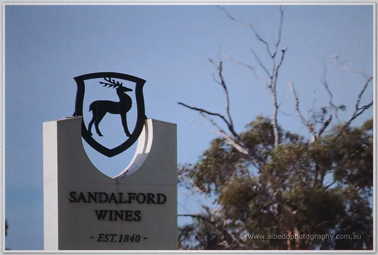Entrance sign at Sandalford Wines crowned by a black stag crest against a clear blue sky and leafless branches