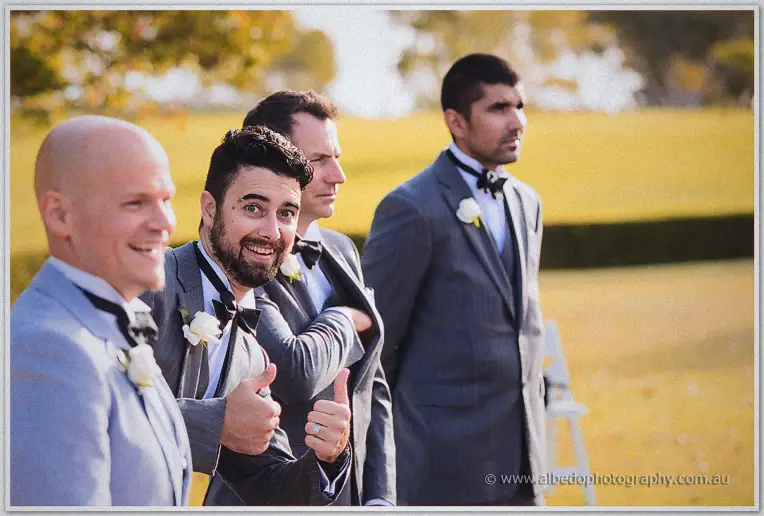 Bearded groomsman giving double thumbs-up while the waiting groomsmen smile on the lawn before the ceremony