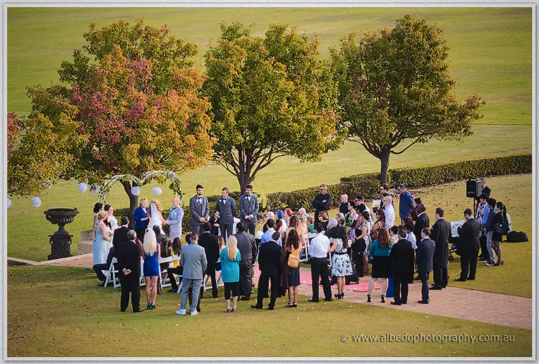 Elevated view of the garden ceremony, guests crowding the lawn around Jasmine and Michael under autumn trees