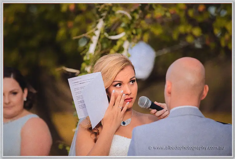 Jasmine wipes away a tear while reading her vows beneath the garden arbour, Michael watching on.