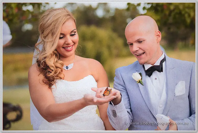 Jasmine and Michael grin at the butterfly perched on their fingers by the lake.