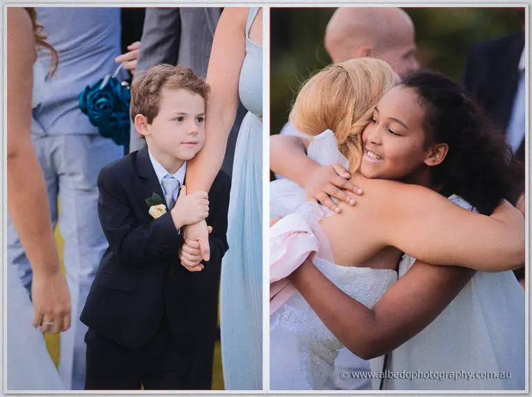 Page boy clutches his uncle's arm while the bride hugs a smiling young guest.