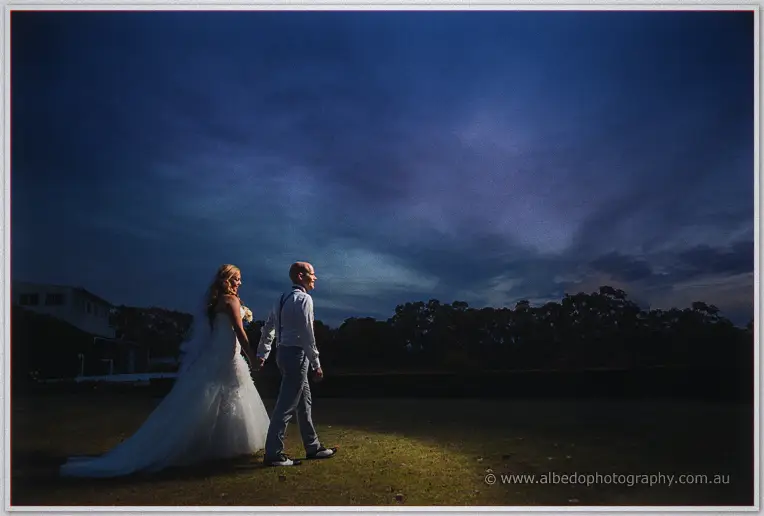 Bride and groom stroll side-lit across the darkening grounds after their winery wedding.