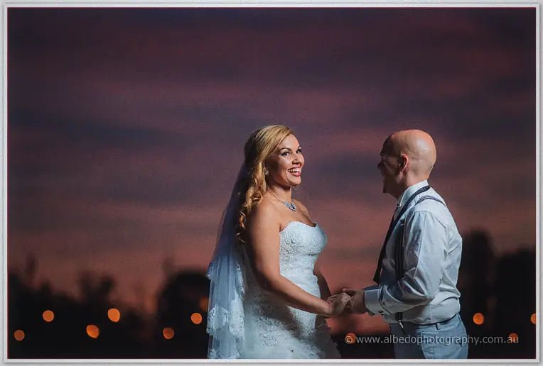 Jasmine laughs as she takes Michael's hands beneath soft pink evening clouds.