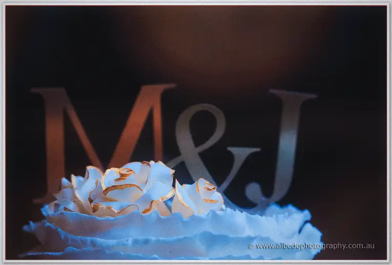 Close-up of the white wedding cake with gold-trimmed roses beneath glowing M and J letters.