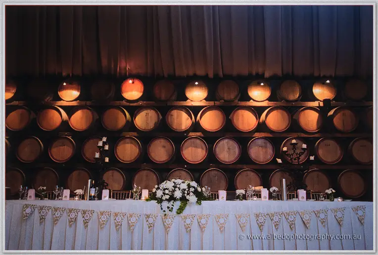 Bridal table with white blooms and bunting set against a wall of glowing oak barrels.