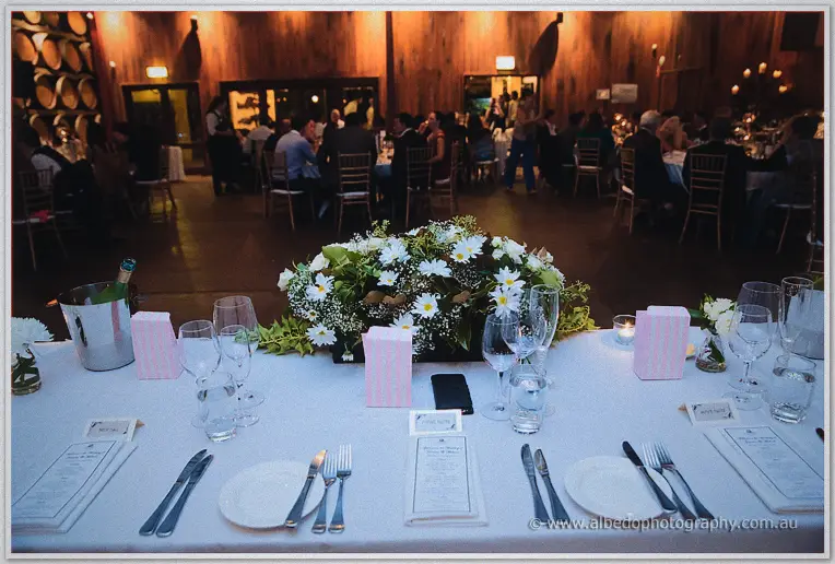 Daisy centerpiece on the bridal table as guests mingle in the timber-lined barrel hall.