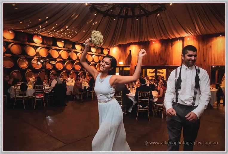 A guest in pale blue whoops with arms raised after catching the bouquet.