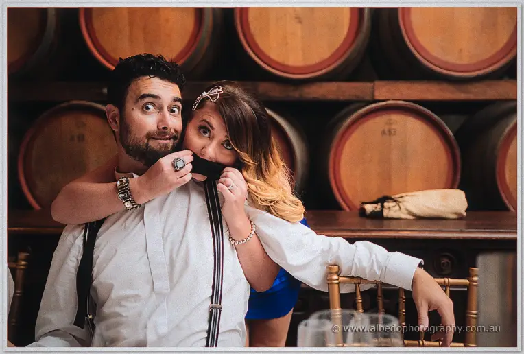 A groomsman pulls a goofy face as a friend in blue playfully tugs his bow tie.
