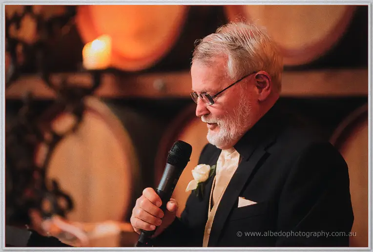 A silver-haired toastmaster in black tie speaks warmly into the microphone.