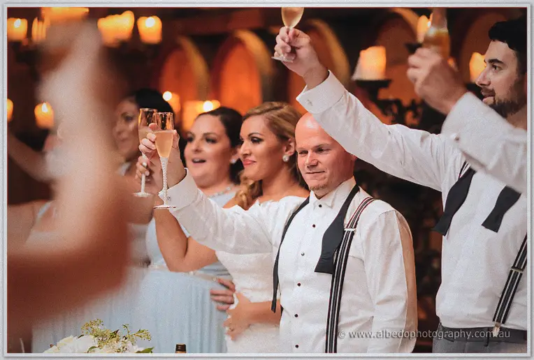 The bridal party raises champagne flutes together during toasts in candlelight.
