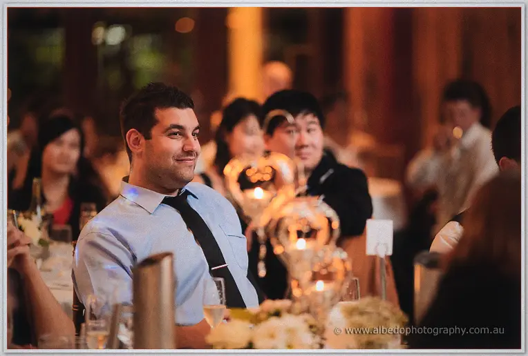 Guests smile over candlelit tables as speeches begin in the timber reception hall.