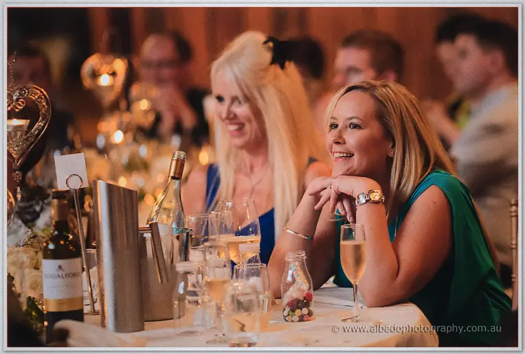 Women in teal and blue listen intently over wine glasses at their dinner table.