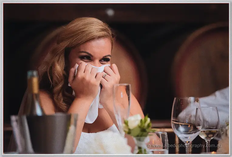 Jasmine presses her napkin to her lips, laughing through happy tears during the toasts in the barrel room.