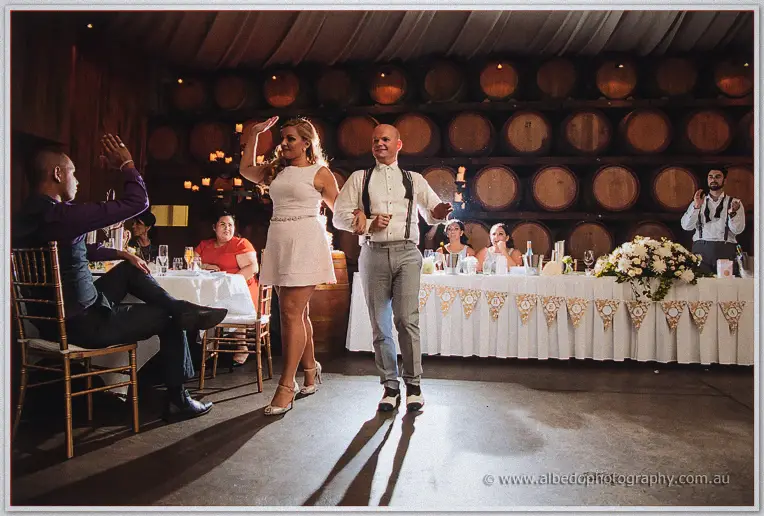 Jasmine and Michael strut hand in hand across the dance floor, guests cheering from the bridal table.