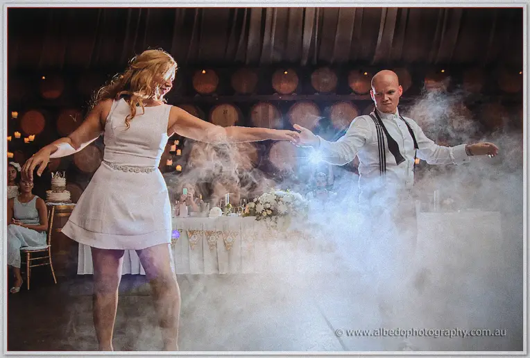 Backlit by a flare and swirling fog, Jasmine spins toward Michael mid first dance in the barrel hall.