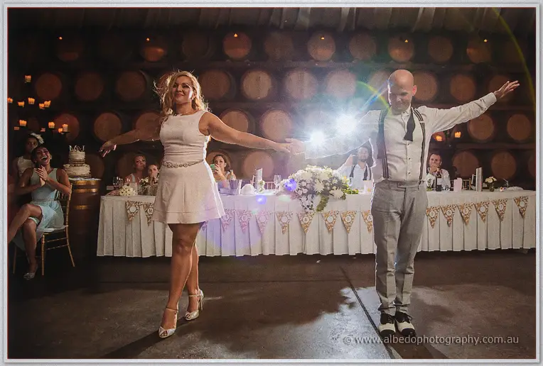 Arms flung wide, Jasmine and Michael hold their dance pose as laughing guests watch from the banquet table.