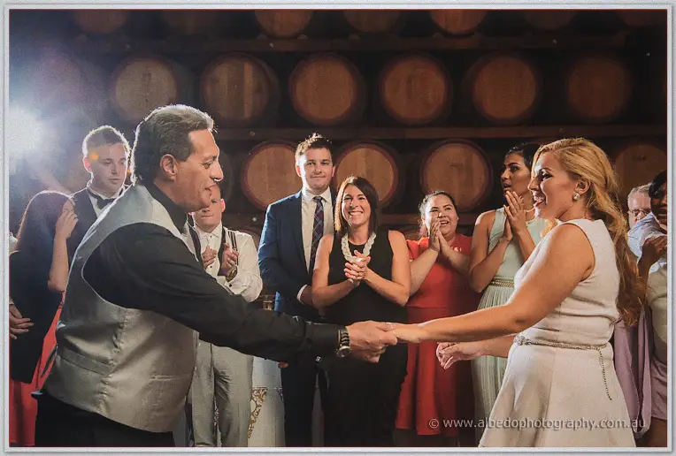 Jasmine dances with an older relative as clapping guests ring the floor in the candlelit barrel room.