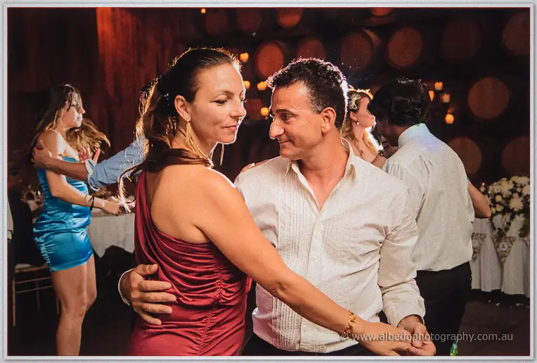 Guests in cocktail wear dance close under the timber rafters as the reception winds on.