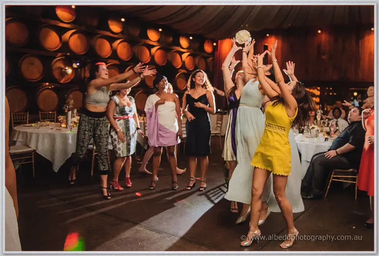 Bridesmaids leap with outstretched hands to catch the tossed bouquet on the dance floor.