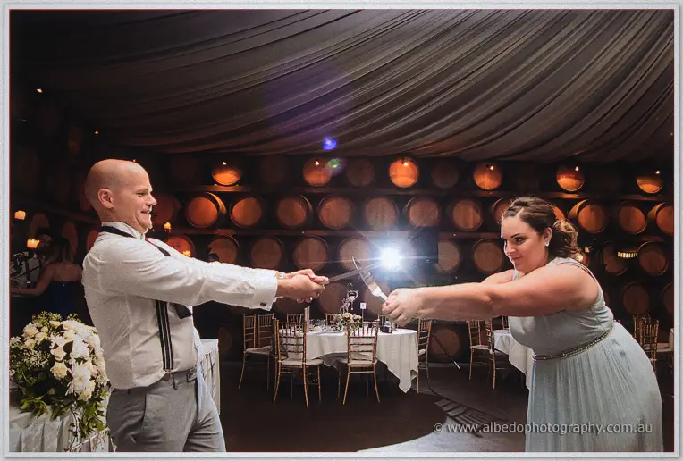 A groomsman and bridesmaid mime a sword fight with cutlery between the reception tables.