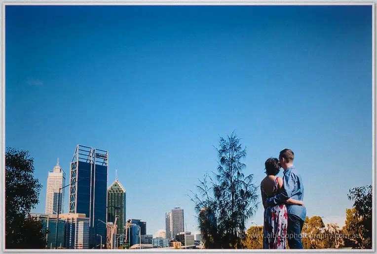 Loan and Alex watch the city skyline together under a vast clear blue afternoon sky